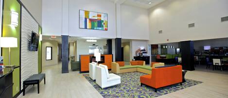 A spacious lobby with a high ceiling, a reception desk, seating area with sofas, and a patterned carpet.