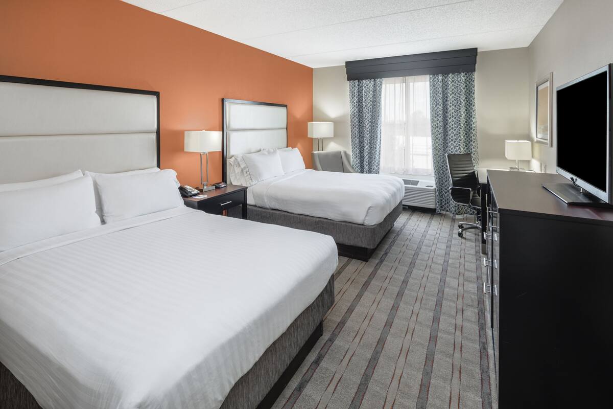 A hotel room with two beds, a desk, a television, and a window with curtains.