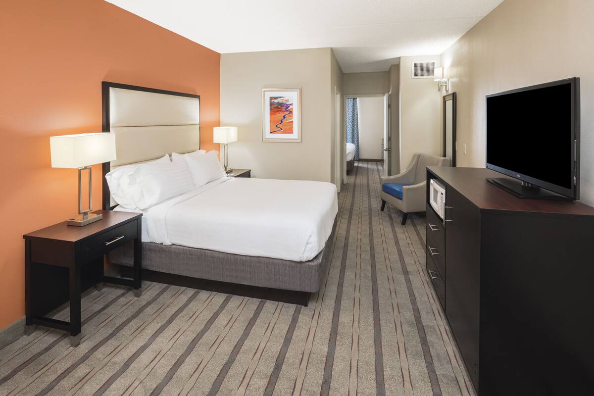 A hotel room with a bed, bedside tables, a TV, a desk, and a chair.