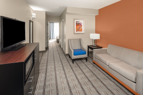 A hotel room with a flat-screen TV, a gray sofa, a blue chair, a lamp, and a framed artwork on the wall. - Holiday Inn Express & Suites Atlanta NE - Duluth by IHG (Duluth)