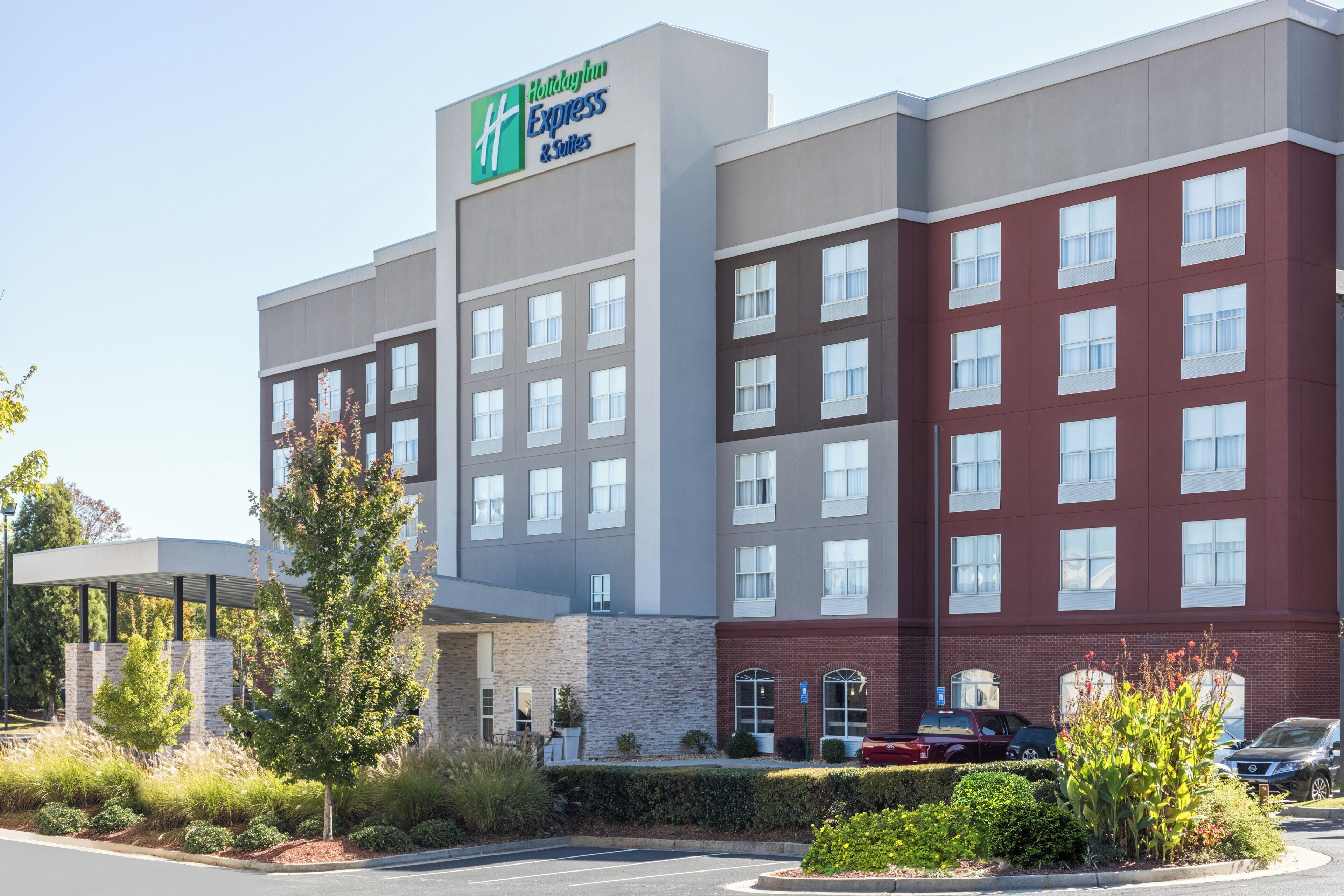 A Holiday Inn Express & Suites hotel with a modern design, featuring a mix of brick and stucco exterior, multiple windows, and a parking area with vehicles.