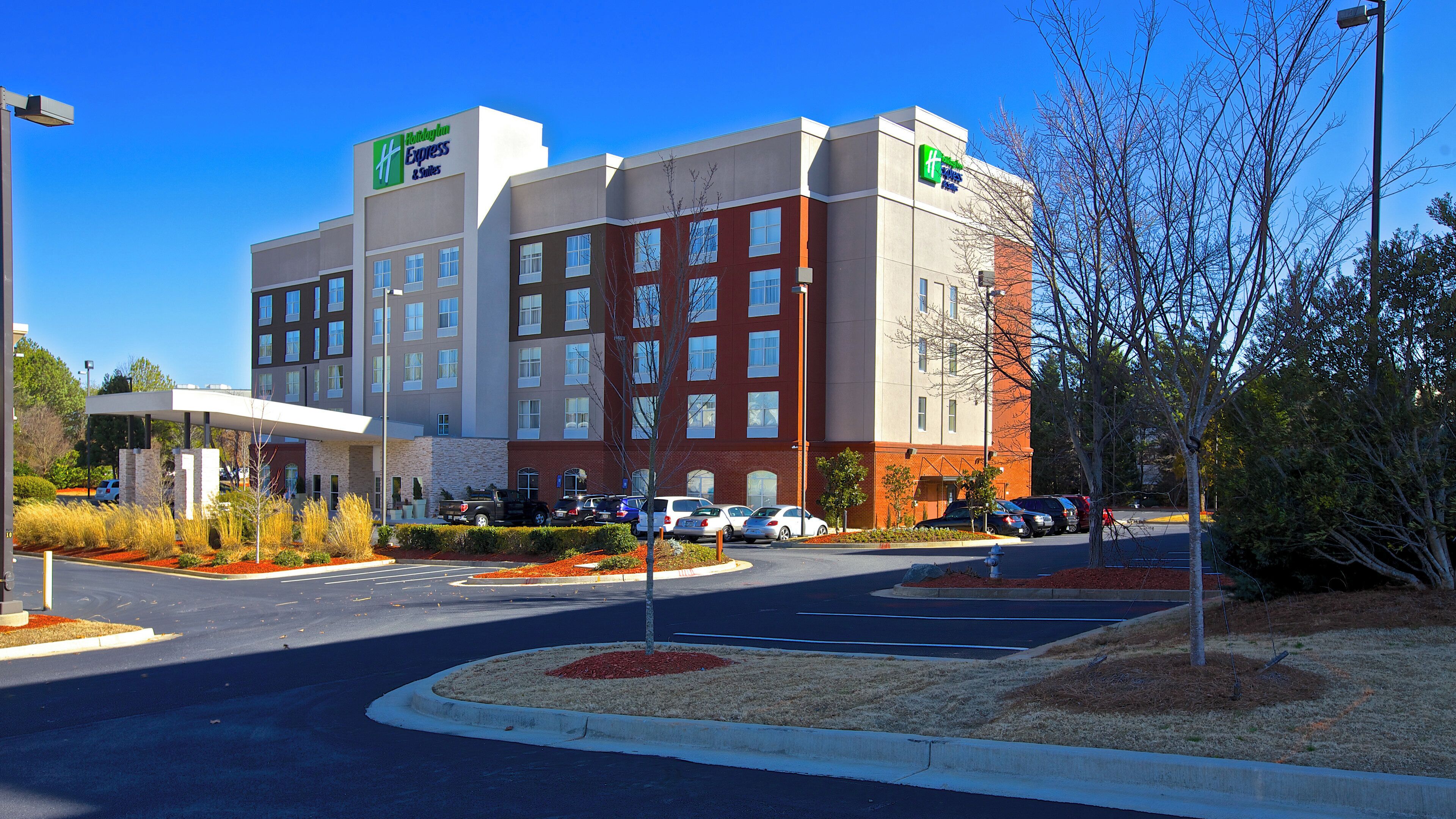 A hotel with a modern design, multiple parking spaces, and a landscaped area with shrubs and trees.