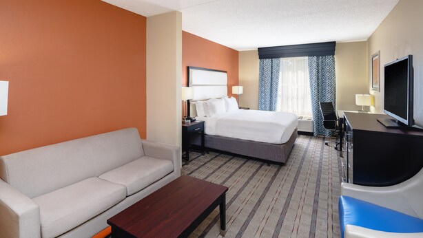 Habitación de hotel con cama, sofá, escritorio, televisor y ventana con cortinas.