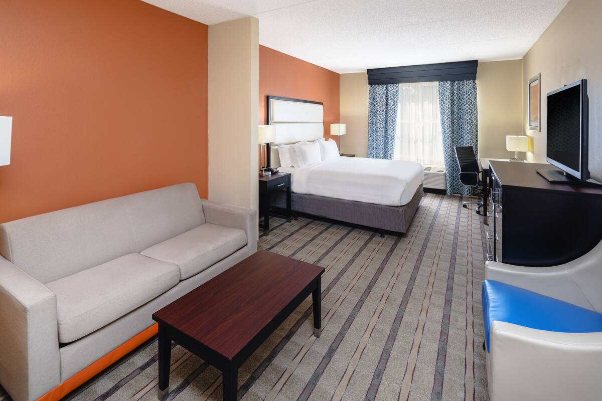A hotel room with a bed, a sofa, a desk, a TV, and a window with curtains.