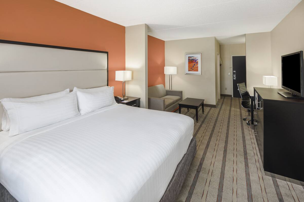 A hotel room with a large bed, a desk, a chair, a TV, and a lamp.