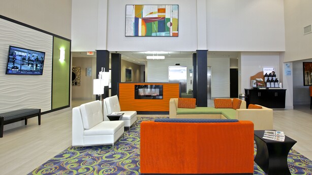 A lobby with a reception desk, seating area with sofas and armchairs, a patterned rug, and a television screen. - Holiday Inn Express & Suites Atlanta NE - Duluth by IHG (Duluth)