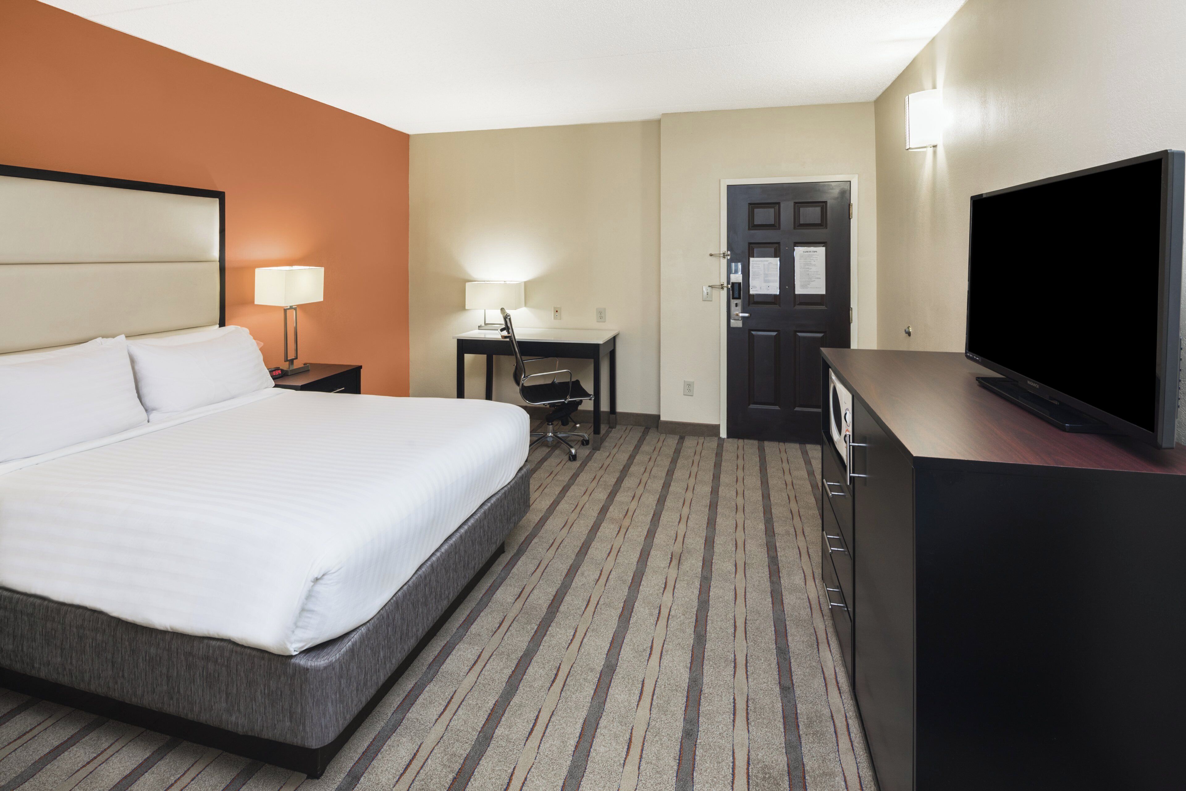 A hotel room with a bed, a desk, a chair, a television, and a door.