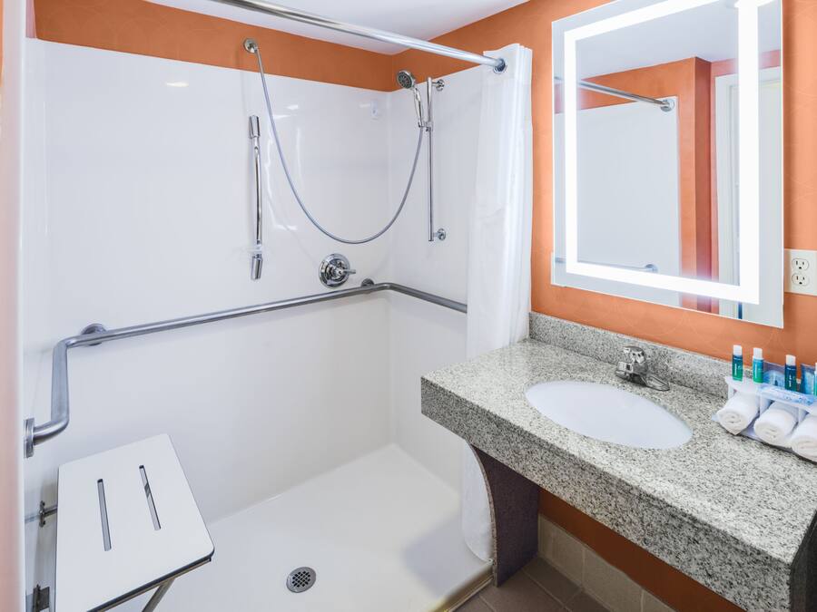 A modern bathroom with a shower, grab bar, sink, and a mirror.