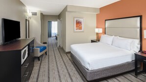 Ein Hotelzimmer mit einem großen Bett, einem Fernseher, einem Schreibtisch mit Computer und einem Badezimmer.