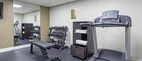 Un gimnasio con cinta de correr, mancuernas y un espejo.