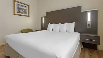 A modern hotel room with a large bed, a nightstand, a chair, and a framed picture on the wall.