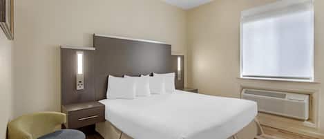 Una habitación de hotel con una cama grande, mesitas de noche, una silla, una ventana con persianas y un aire acondicionado instalado en la pared.