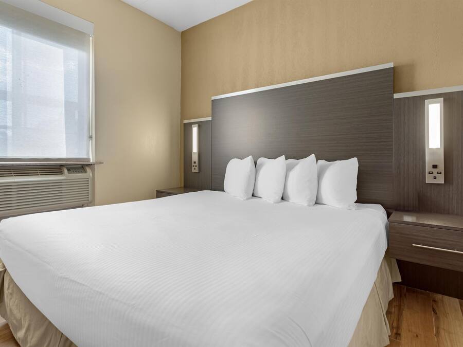 A modern hotel room with a large bed, a bedside table, a nightstand, and a wall-mounted light fixture.