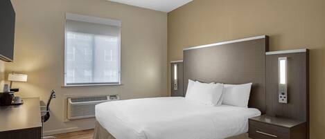 Ett modernt hotellrum med en stor säng, sängbord, ett skrivbord och ett fönster med persienner.