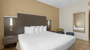 Una habitación de hotel moderna con una cama grande, mesitas de noche, un espejo y una pequeña zona de estar.