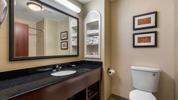 A bathroom with a sink, mirror, toilet, and towel storage.