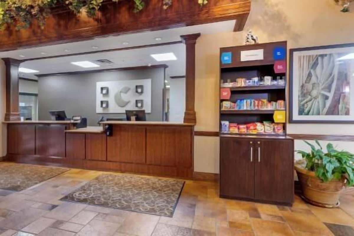A reception area with a wooden reception desk, a wall-mounted information board, a shelf with snacks, and a potted plant.