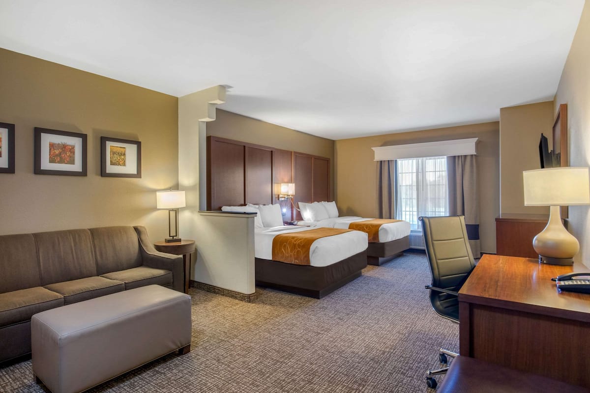 A hotel room with two beds, a sofa, a desk, and a chair.