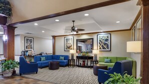 A spacious lobby with a blue sofa, green sofa, and a coffee table. There are potted plants and framed artwork on the walls. - Comfort Suites Marshall (Marshall)