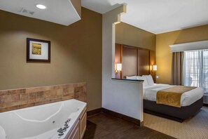 A hotel room with a large bathtub, a bed with a headboard, a bedside table, and a window with curtains. - Comfort Suites Marshall (Marshall)