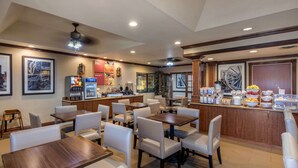 A hotel dining area with multiple tables and chairs, a bar counter with various food items, and a large decorative wheel on the wall. - Comfort Suites Marshall (Marshall)