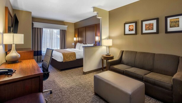 A hotel room with a bed, desk, chair, sofa, and ottoman. There are three framed pictures on the wall. - Comfort Suites Marshall (Marshall)