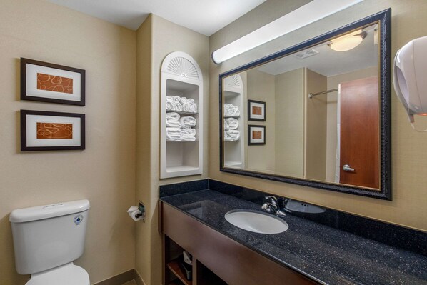 A bathroom with a white toilet, a sink with a black countertop, a large mirror, and towel racks with folded towels. - Comfort Suites Marshall (Marshall)