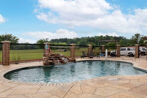 A swimming pool with a stone border, a waterfall feature, and a fenced area with lounge chairs. - Comfort Suites Marshall (Marshall)