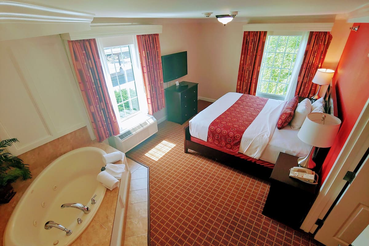 A hotel room with a large bed, a bathroom with a bathtub, and a TV.