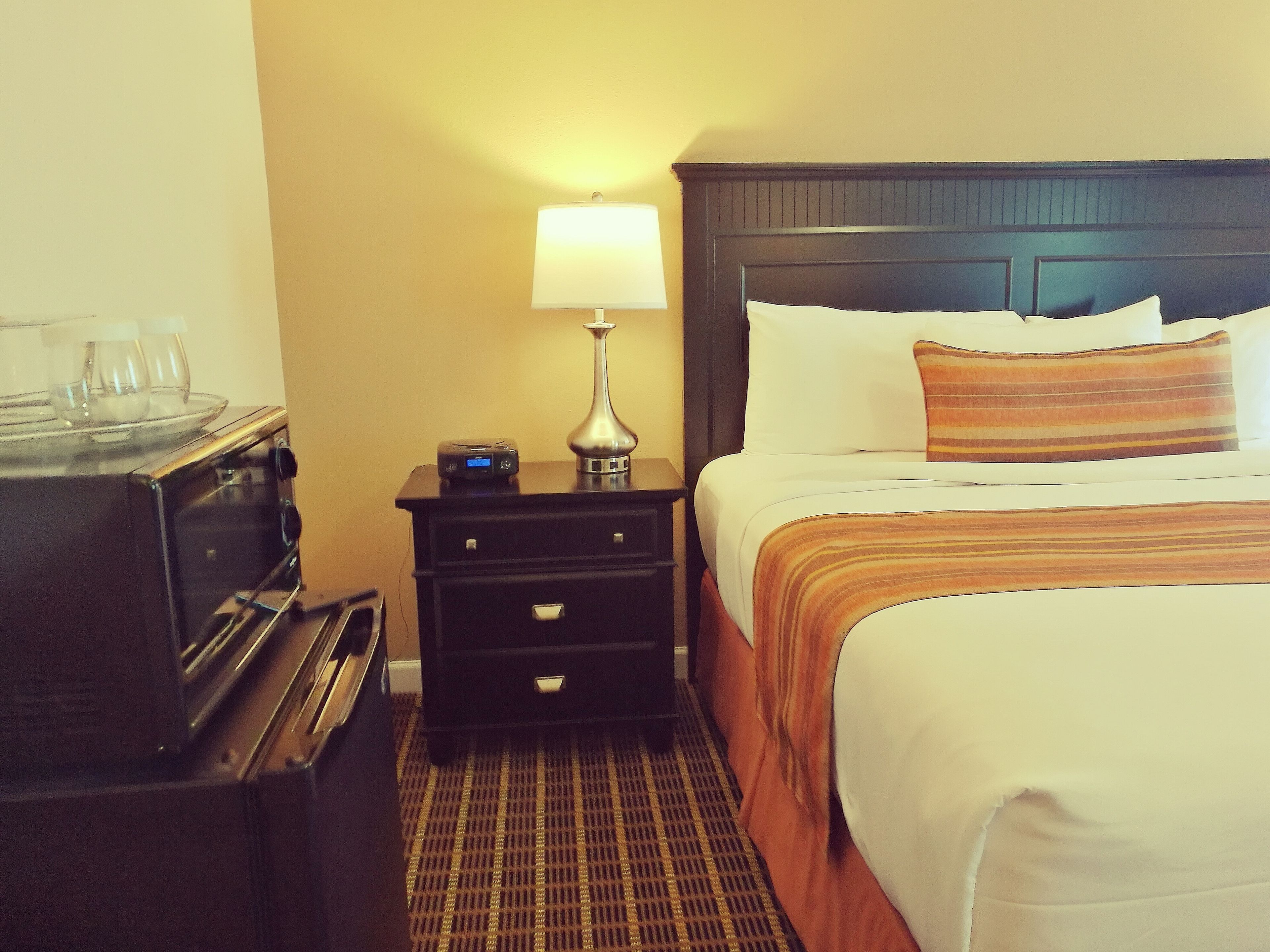 A hotel room with a bed, a nightstand, a lamp, and a microwave.