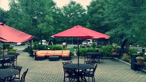 An outdoor patio area with brick flooring, red umbrellas, and outdoor seating. - The Wilshire Grand Hotel (West Orange)