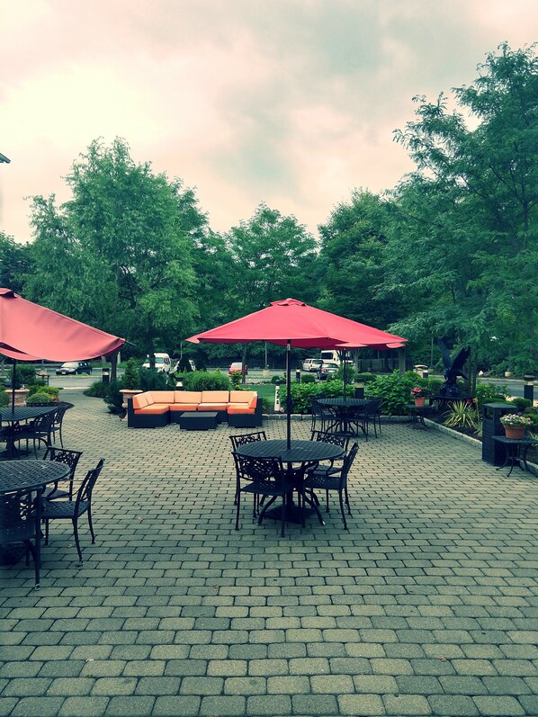 Un patio al aire libre con suelo de ladrillo, sombrillas rojas y mobiliario exterior.