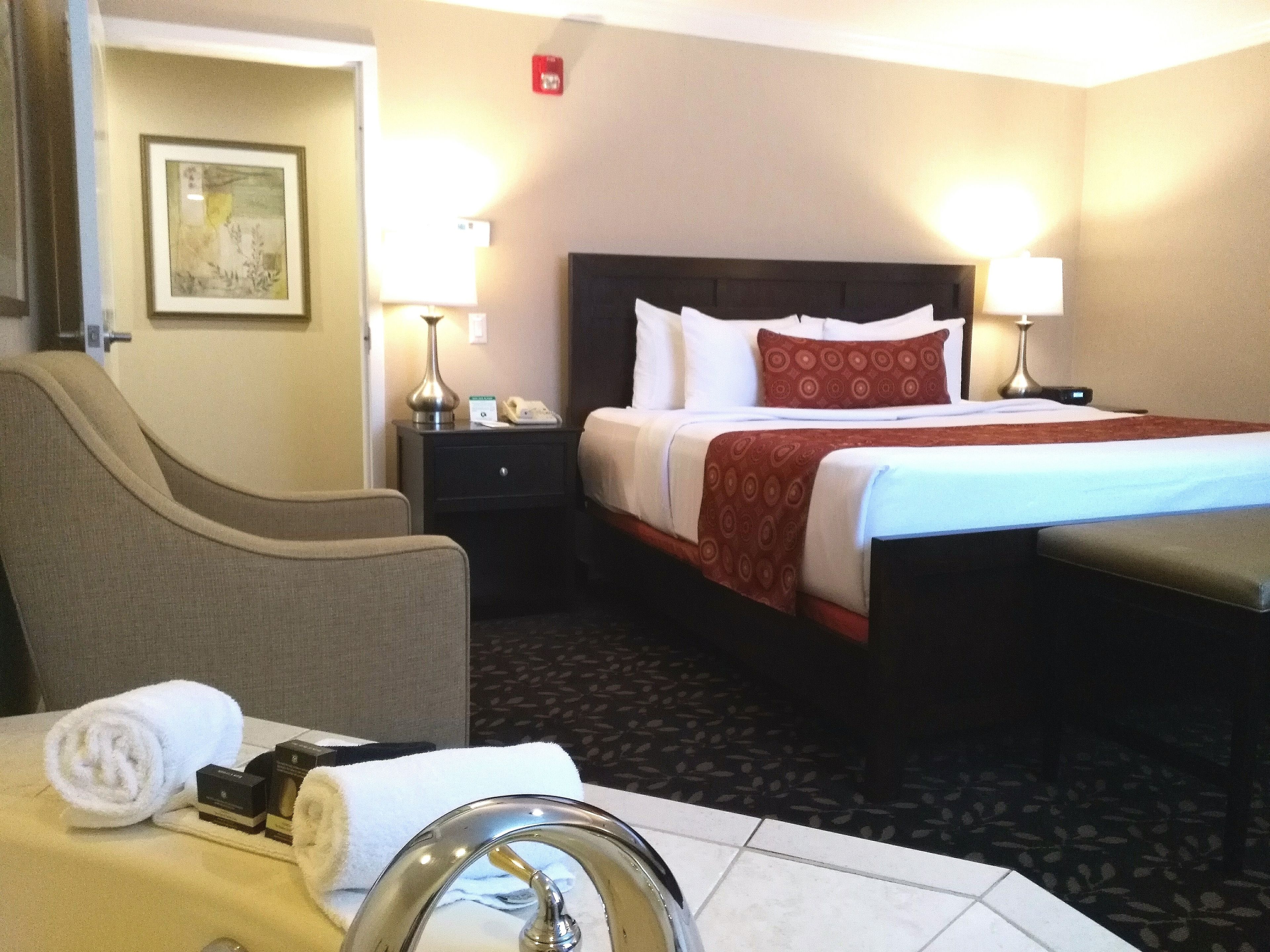 A hotel room with a bed, bedside tables, a chair, a bathroom with a sink, and a towel.