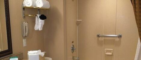 A bathroom with a sink, toilet, and bathtub. There is a towel rack with towels and a hand dryer. A mirror is mounted on the wall above the sink.