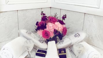 A bathroom with a white marble sink, a bouquet of pink and purple flowers, and two rolled towels.