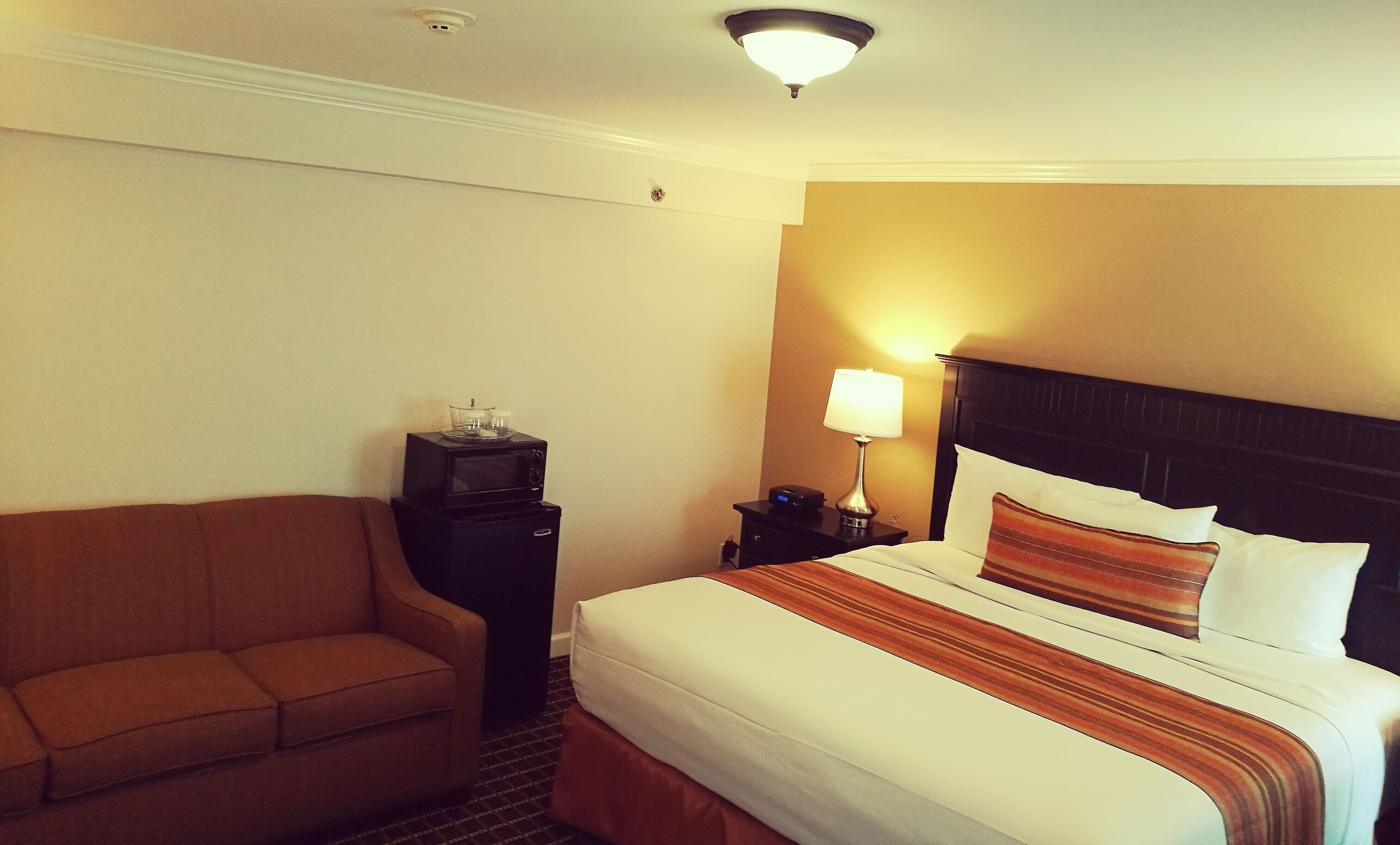 A hotel room with a bed, a nightstand, a lamp, a TV, and a sofa.