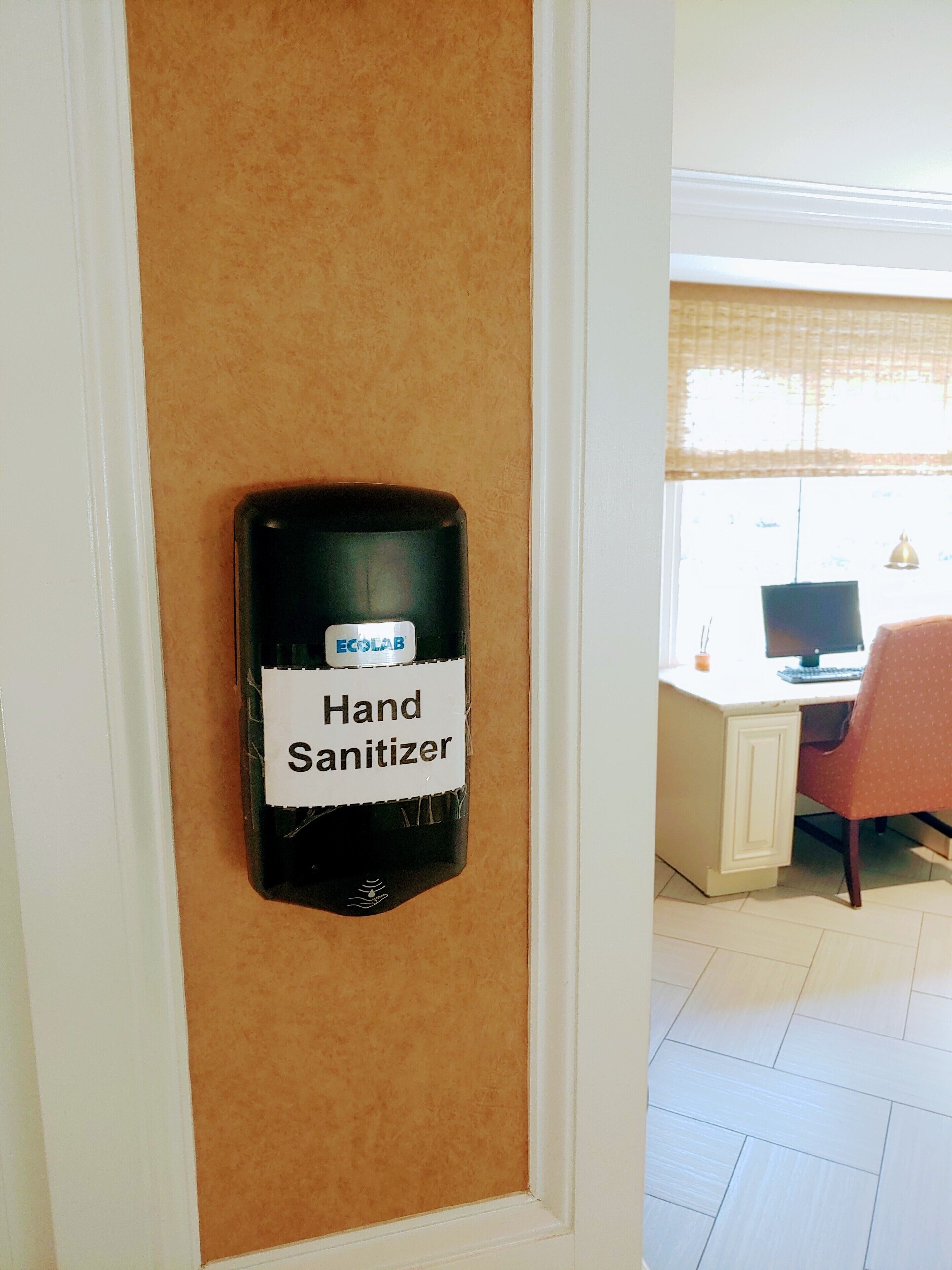 A hand sanitizer dispenser mounted on a door with a beige textured wall.
