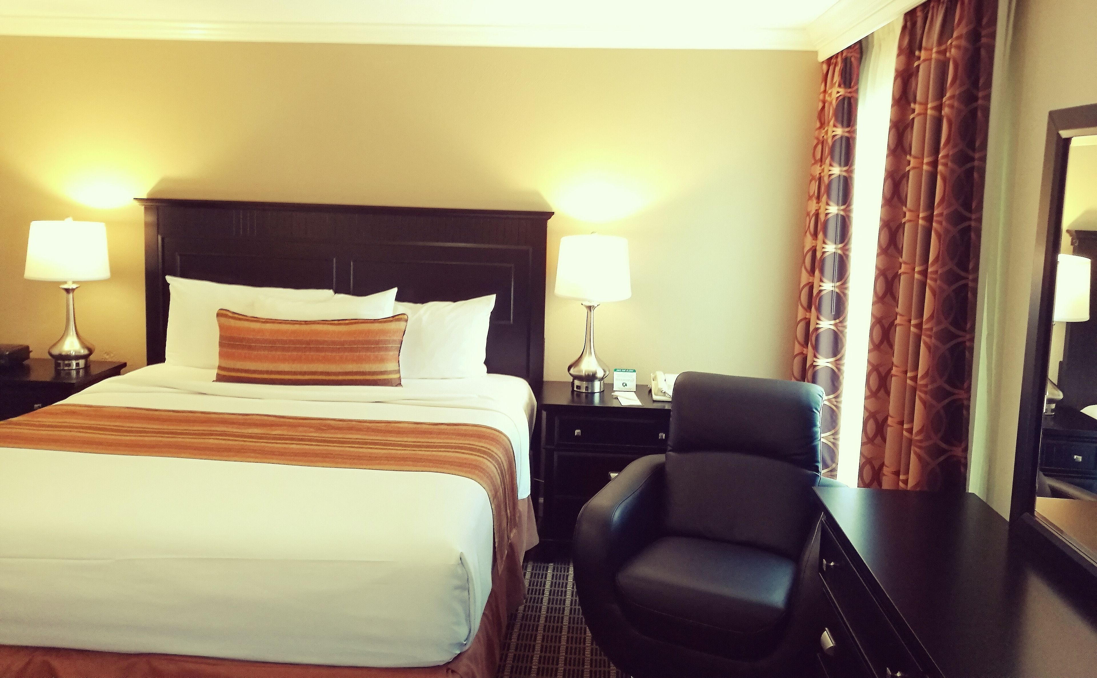 A hotel room with a bed, two bedside lamps, a chair, a nightstand, and a mirror.