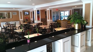 A hotel lobby with a reception desk, multiple seating areas, and a television screen. - The Wilshire Grand Hotel (West Orange)