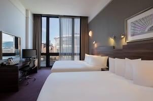 Habitación de hotel con dos camas, un escritorio con televisor y un ventanal con cortinas.