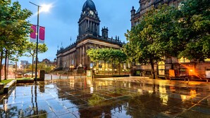 A historic building with a prominent clock tower, surrounded by trees and a wet pavement. - Leonardo Hotel Leeds  (Leeds)