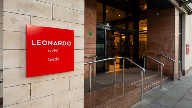 The exterior of the Leonardo Hotel in Leeds, featuring a prominent red sign, a glass entrance, and a set of metal stairs leading up to the door. - Leonardo Hotel Leeds  (Leeds)