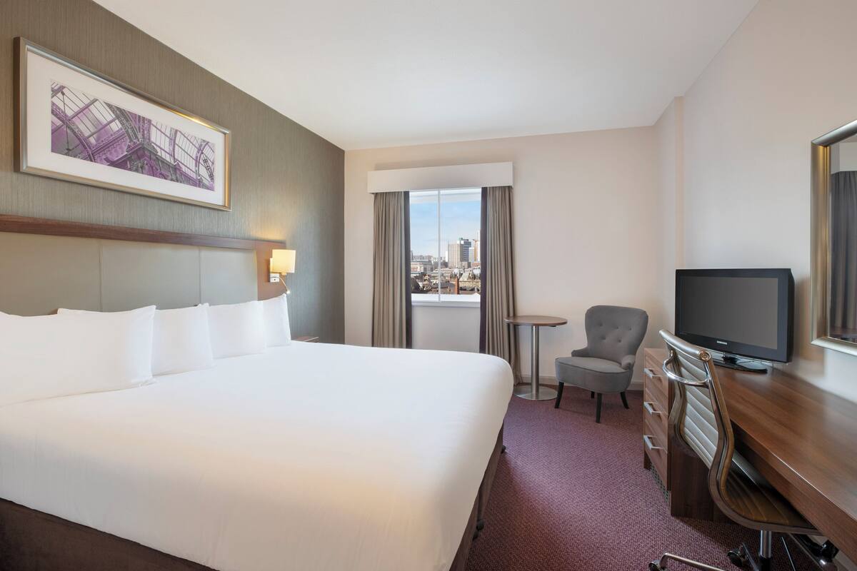 Ein Hotelzimmer mit einem großen Bett, einem Fernseher, einem Schreibtisch und einem Sessel.