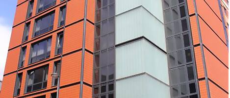 A tall building with a modern design, featuring a mix of orange and grey facades and large windows.