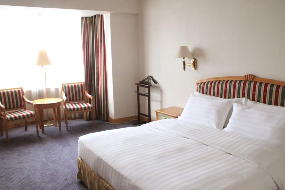A hotel room with a large bed, two striped armchairs, a small round table, a lamp, and a nightstand.