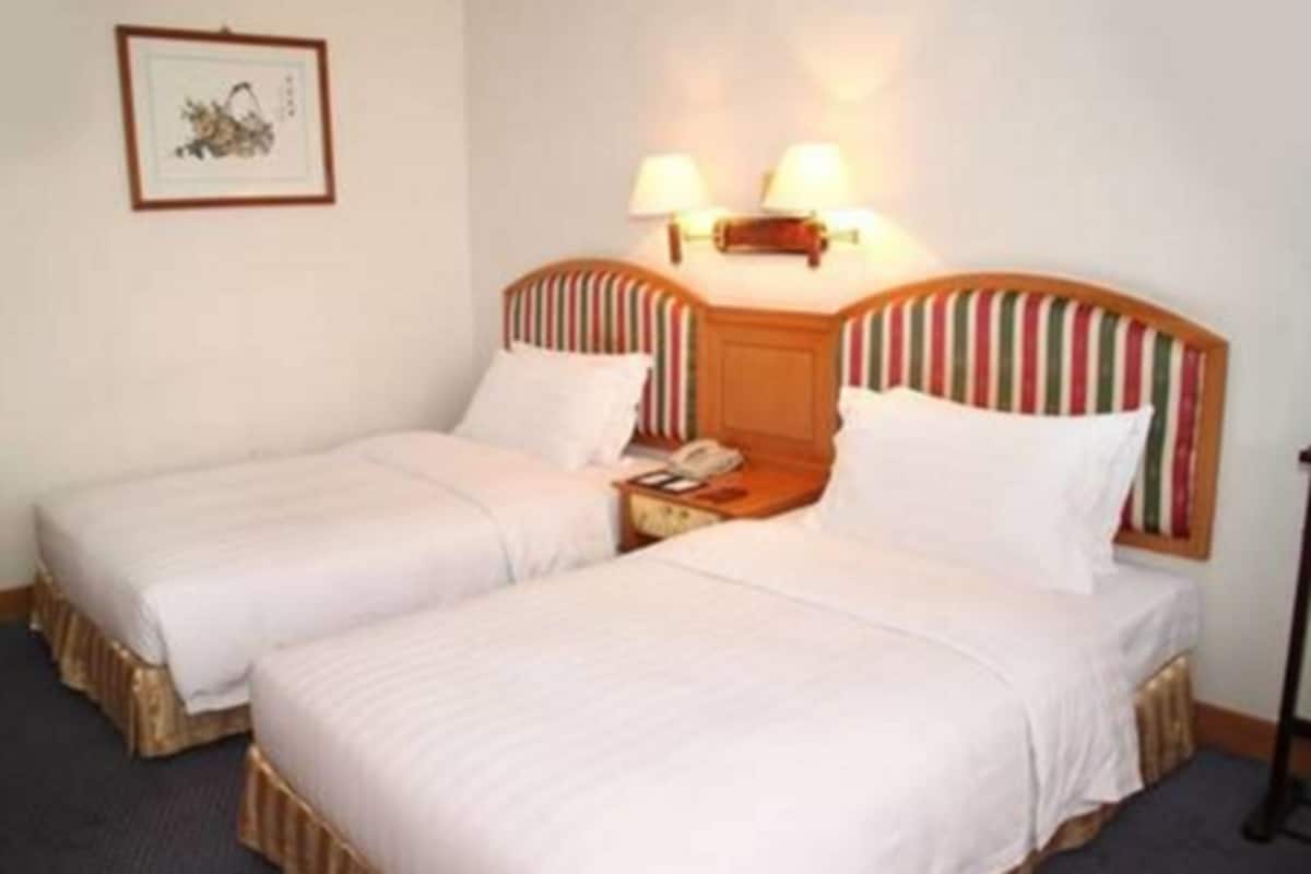 A hotel room with two single beds, a bedside table with a lamp, and a framed picture on the wall.