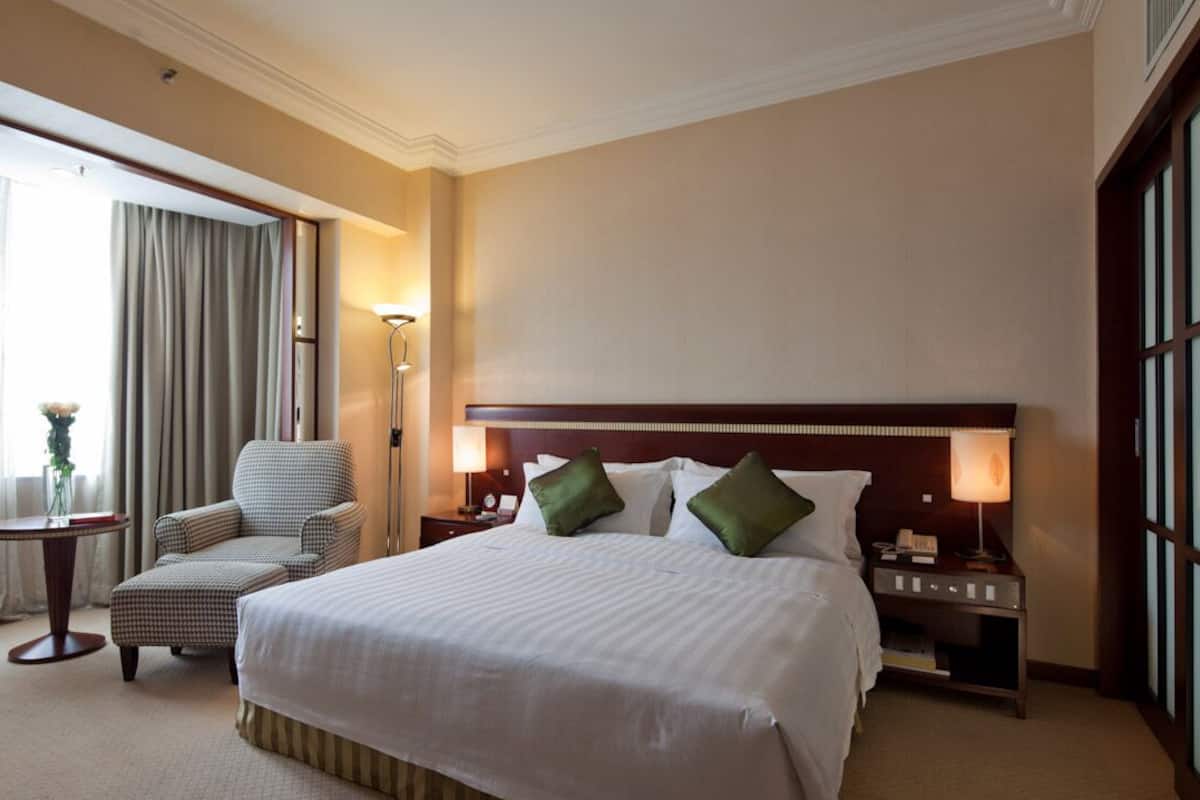 A hotel room with a large bed, a chair, a nightstand, a lamp, and a window with curtains.