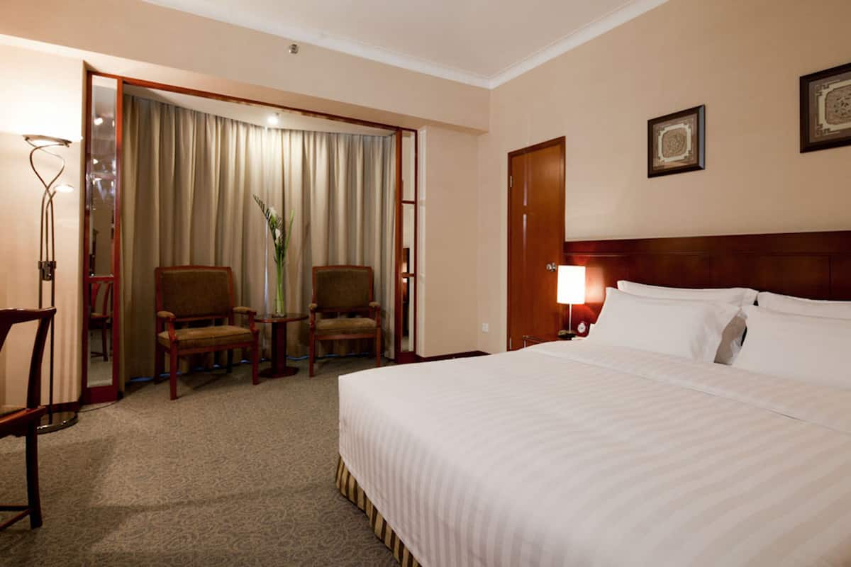 A hotel room with a large bed, two chairs, a desk, a lamp, and a door leading to a balcony.