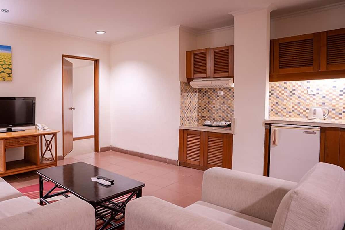 Un espace de vie compact comprenant un canapé, une petite table à manger, un téléviseur et une kitchenette équipée d’un réfrigérateur et d’un four à micro-ondes.