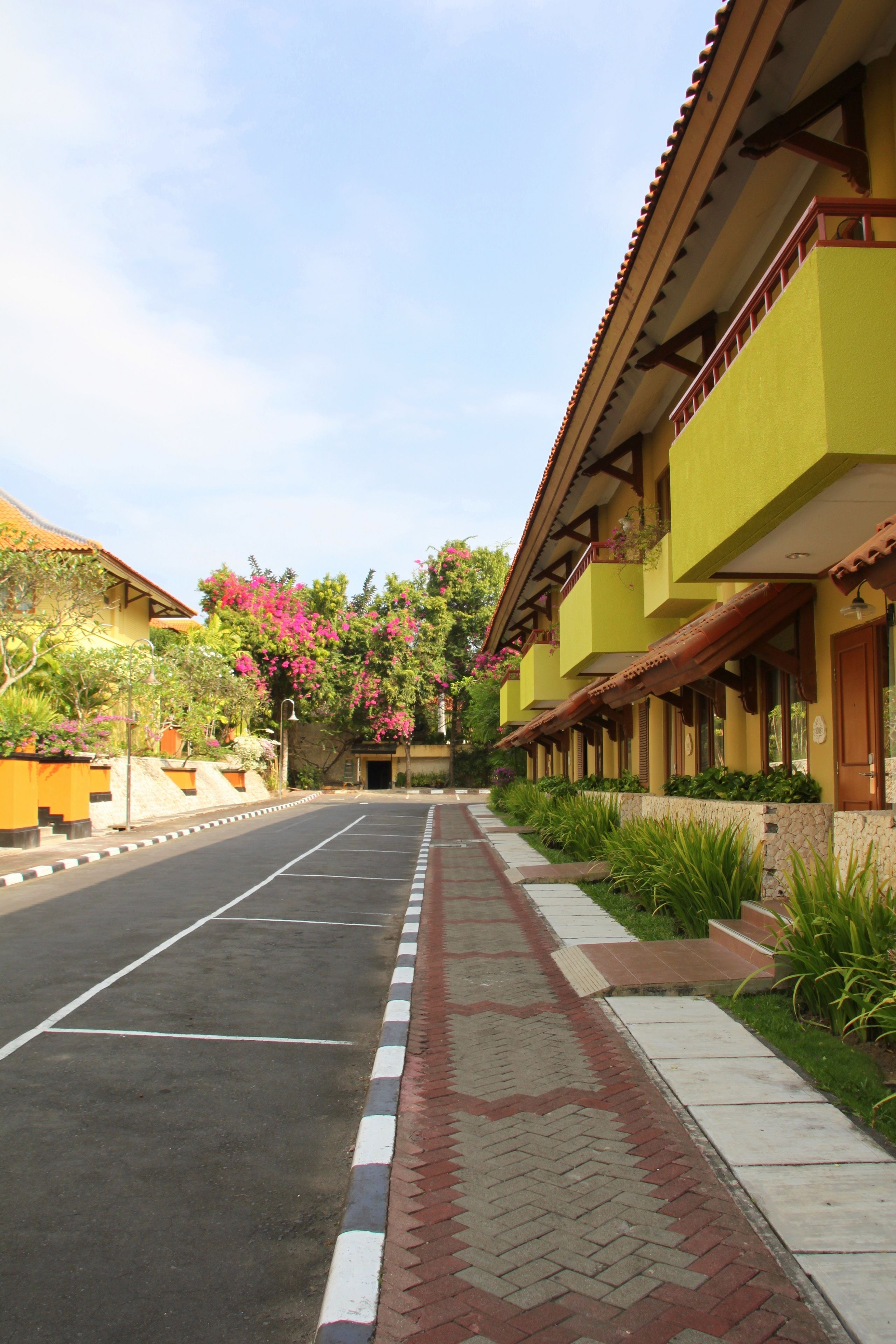 A street view with a row of yellow buildings, a paved road, and a sidewalk with patterned tiles.